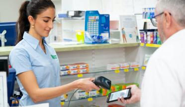 A pharmacy employee scans an electronic prescription from the phone of an elderly male customer