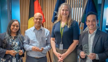 ADHA employees pose in front of three flags.