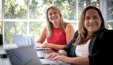 Two women on their laptops looking beyond the camera