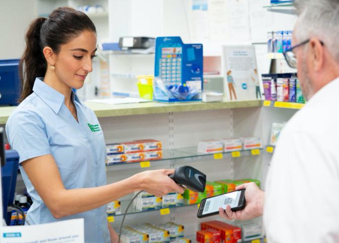 A pharmacy employee scans an electronic prescription from the phone of an elderly male customer