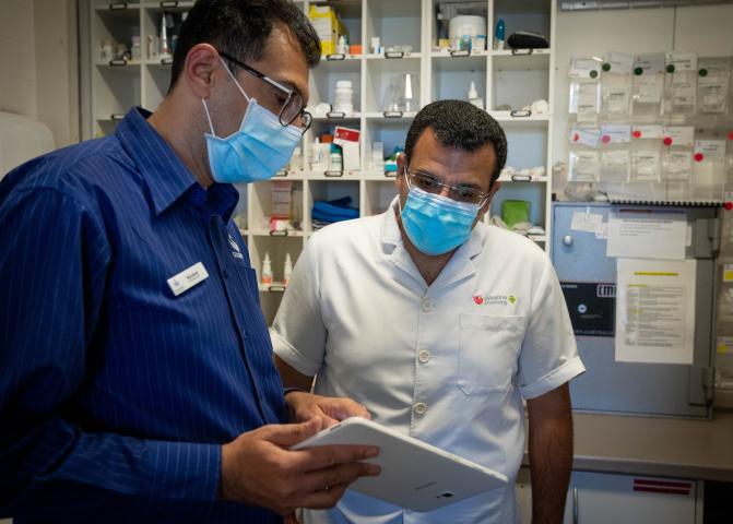 Two people wearing masks looking at a tablet