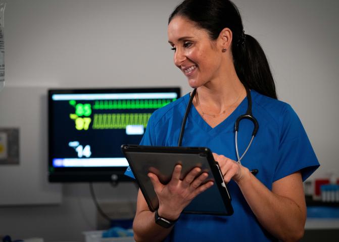 A nurse consults a tablet device while speaking to a patient.