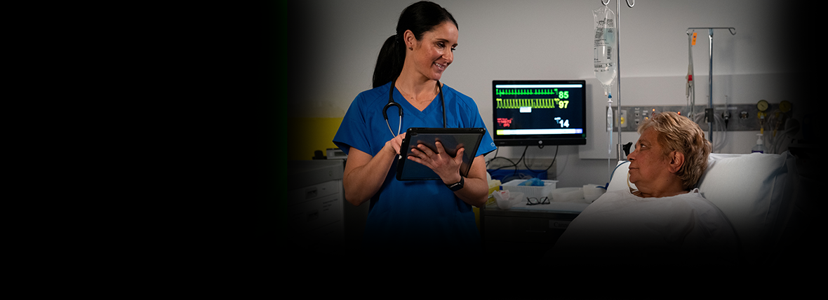 National Digital Health Strategy outcomes, a hospital room setting with a younger female nurse in blue uniform taking vitals of older female patient on bed in white hospital gown