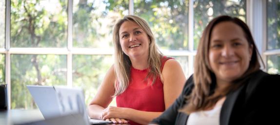 Two women on their laptops looking beyond the camera