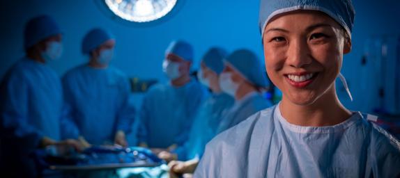 Data-driven outcome - Readily available data to inform decision making about individuals, communities and national issues. Female (of Asian appearance) in hospital surgical room setting with mask and dressed in surgical scrubs, with five female and male surgical staff members blurred in background