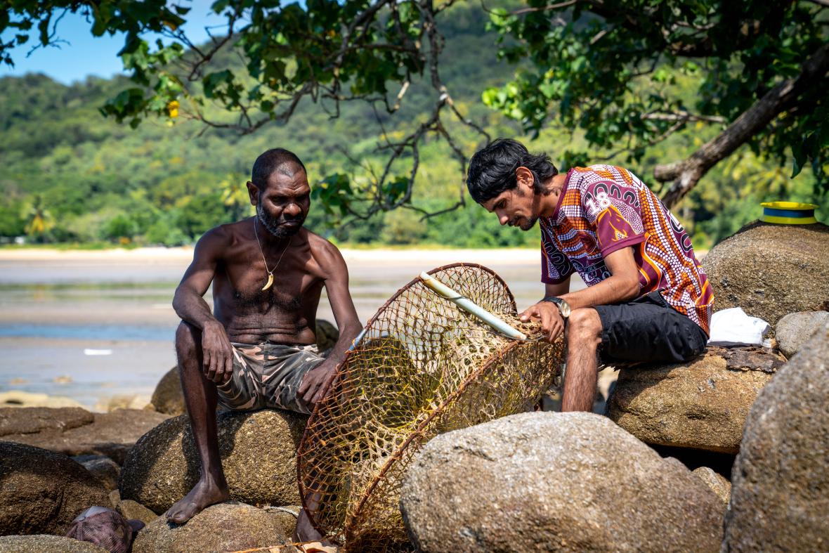 Photo: two men on the rocks by the beach with crab pot