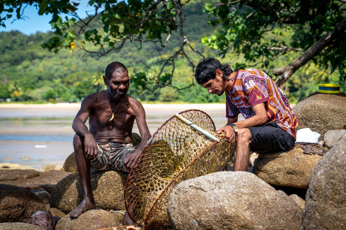 Photo: two men on the rocks by the beach with crab pot