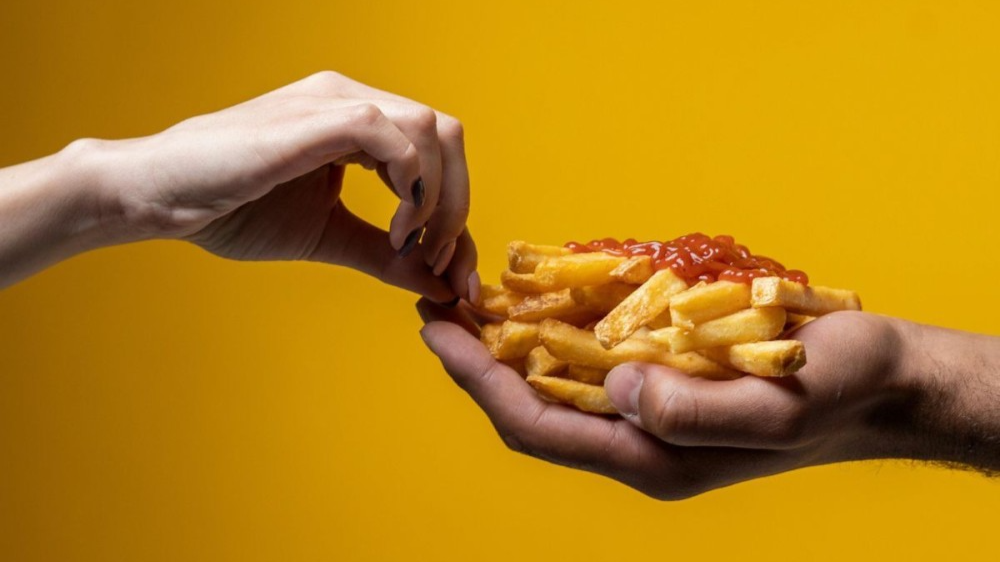 Hands holding fries with tomato sauce