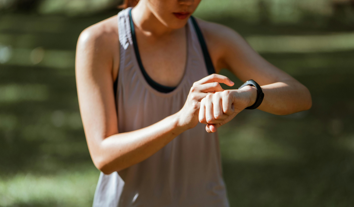 A woman wearing exercise clothes uses her right hand to tap a watch on her left wrist.